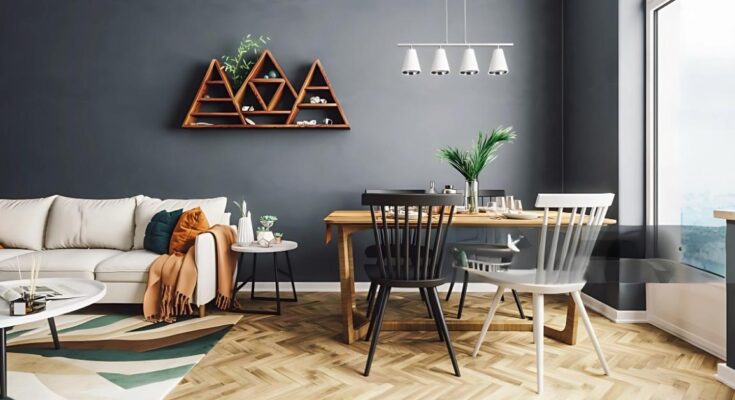 "A cozy living and dining room featuring a modern gray wall, a triangular wooden shelf, a comfortable beige sofa with colorful cushions, and a wooden dining table with mixed-style chairs. The space is well-lit with a window and a hanging light fixture."